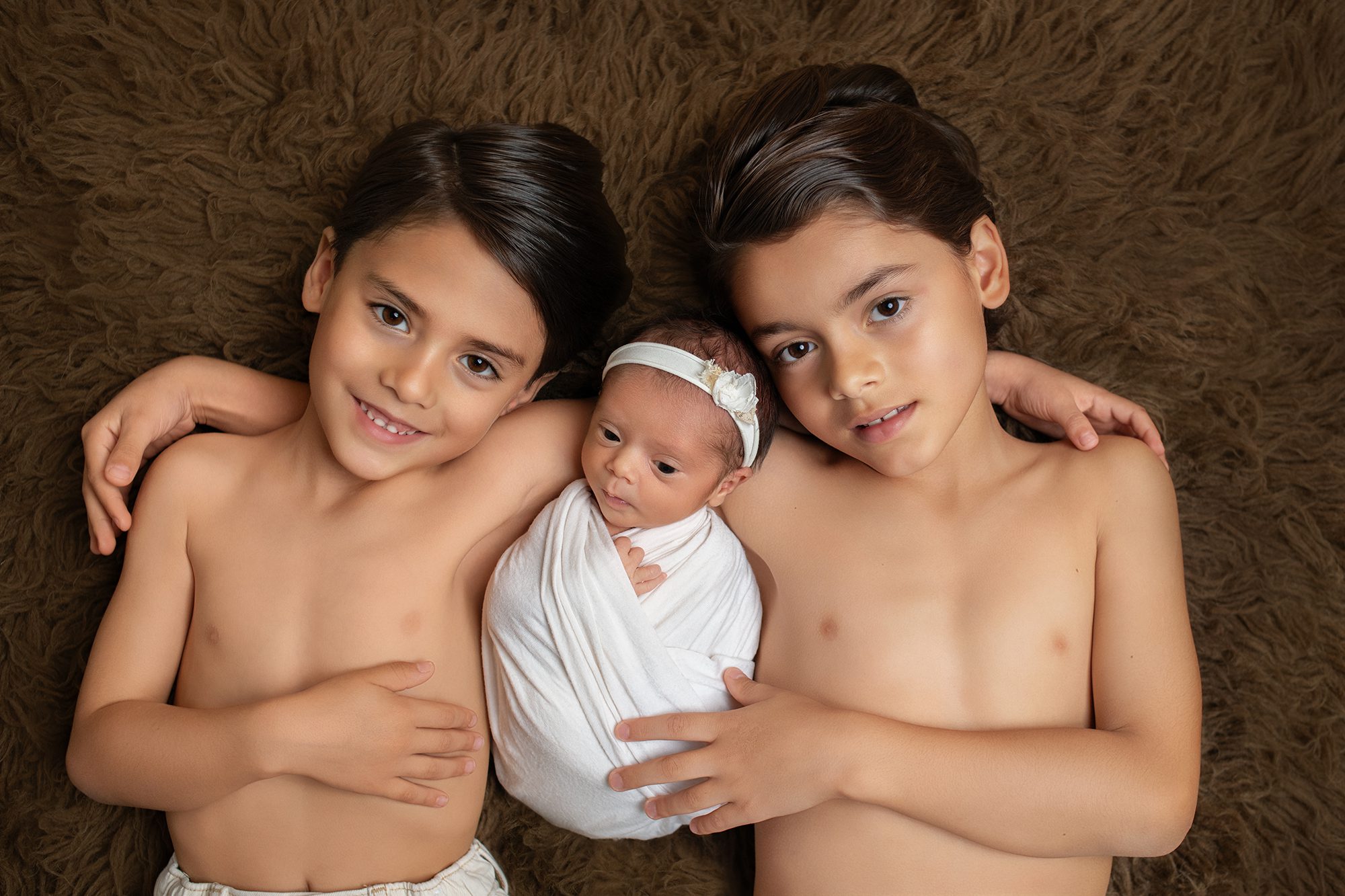 Two big brothers holding their newborn baby sister during a sibling photography session in San Elijo Hills